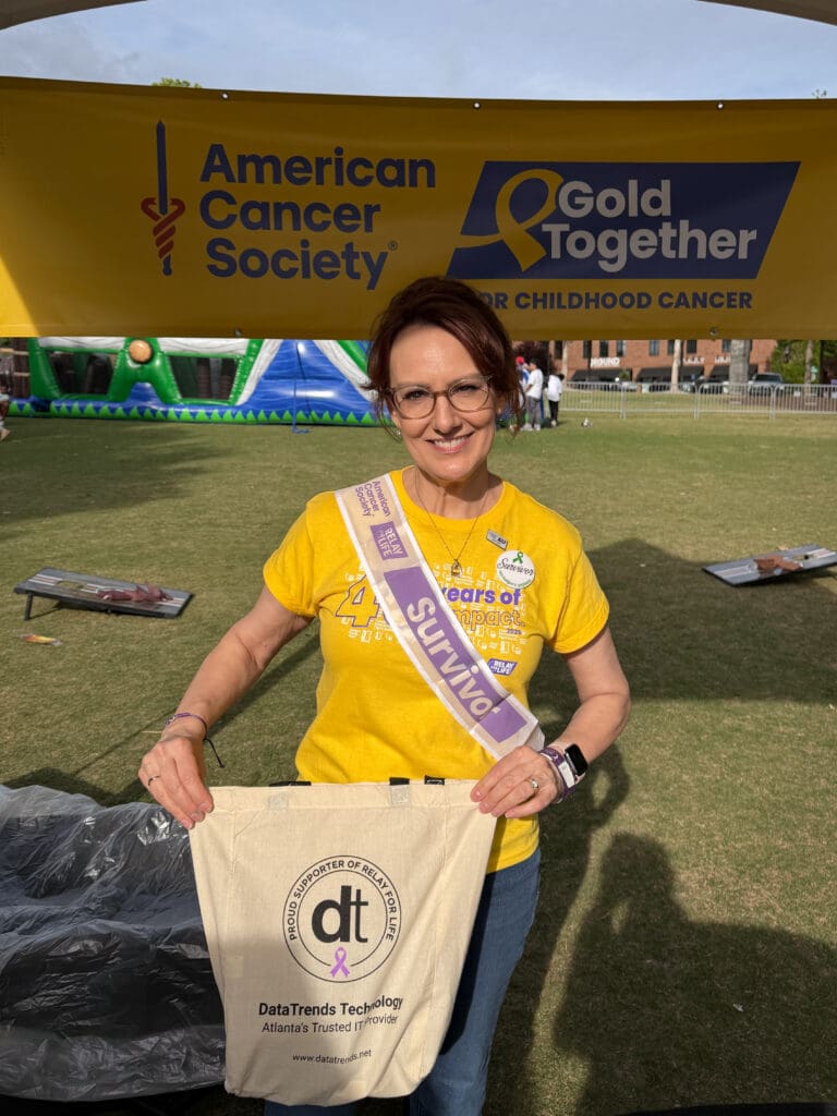 Person wearing "Survivor" sash holding tote under banner